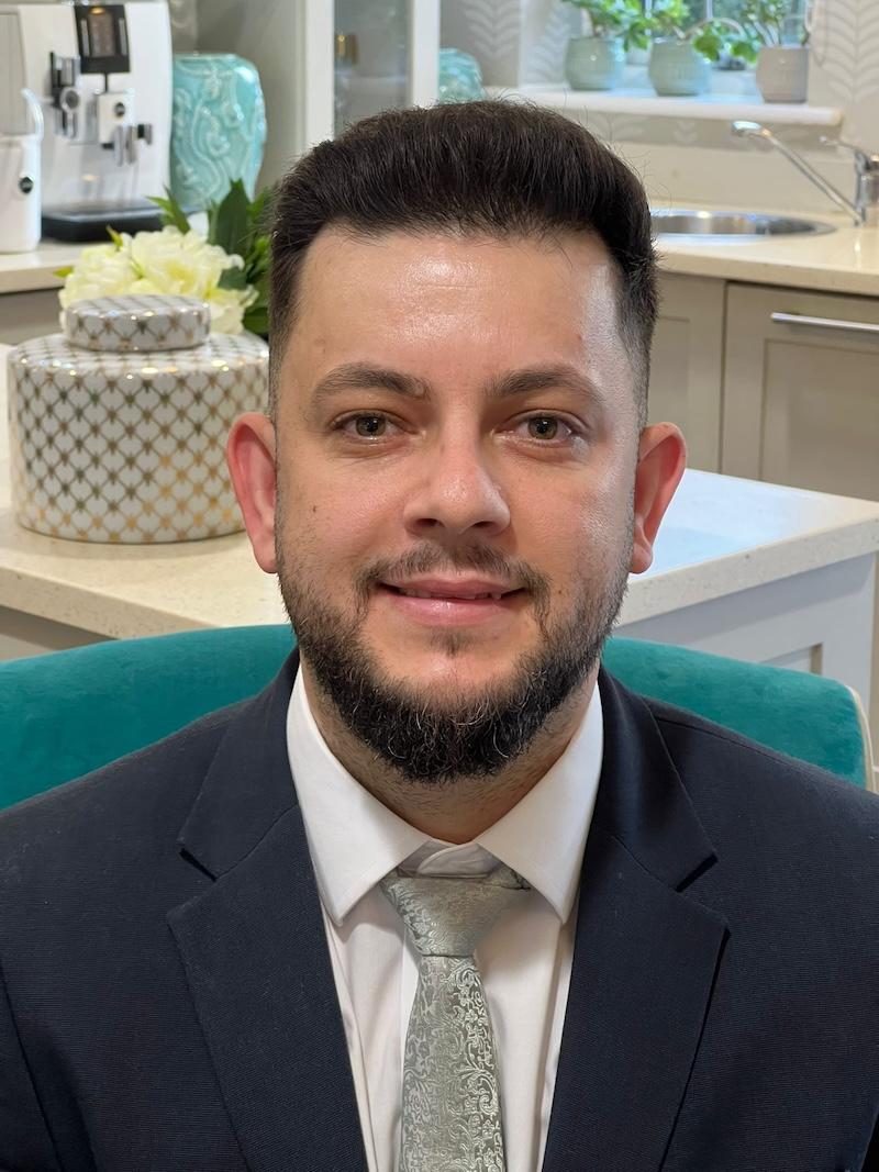 cristian our deputy manager sat on a chair wearing a blue suit and a silver tie