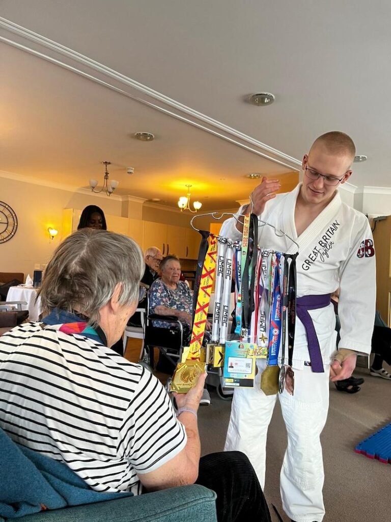 one of our residents being shown medals on a hanger by a member of draco's dojo jui jitzu