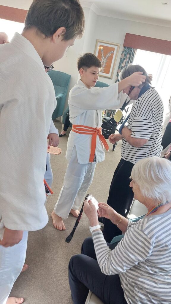one of our visitors from dracos dojo putting a gold medal onto a residents neck
