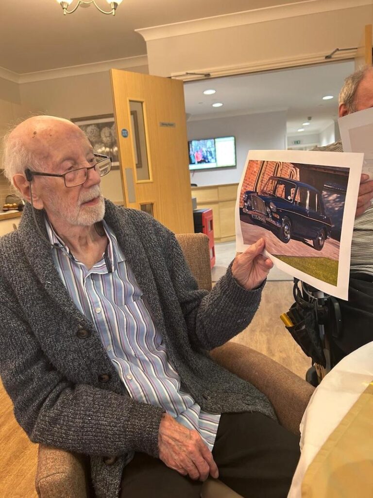 one of our male residents sat in an armchair holding up a photo of a vintage car