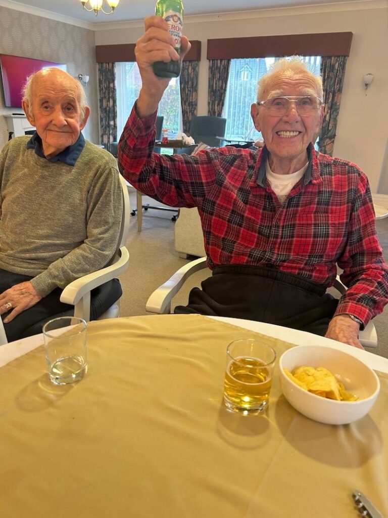 two of our male residents sat together enjoying a beer and some crisps, one holding up a drink
