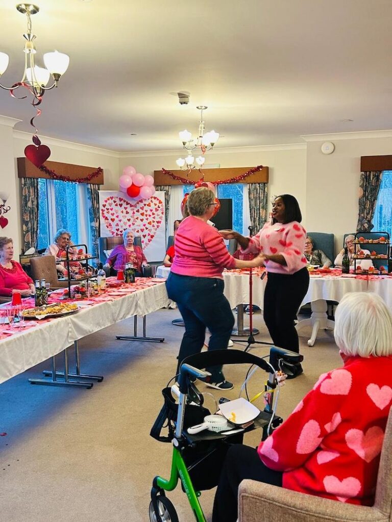 resident and carer holding hands and dancing in our lounge filled with valentines day decorations