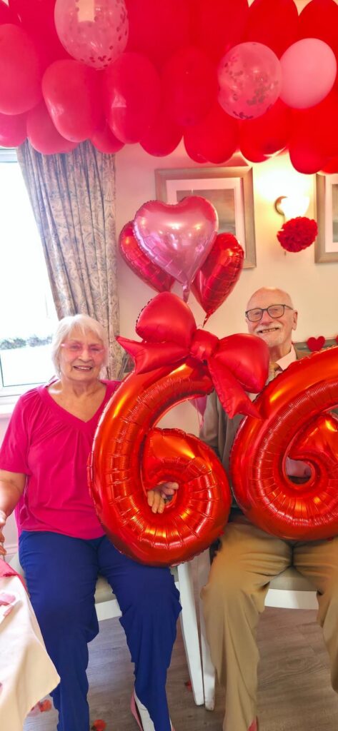 an older man and woman sat together holding 66 balloons for their 66th anniversary