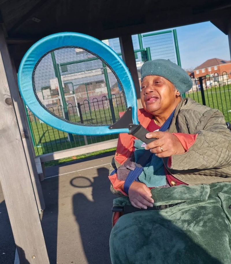 one of our residents sat in a wheelchair holding a blue racket smiling