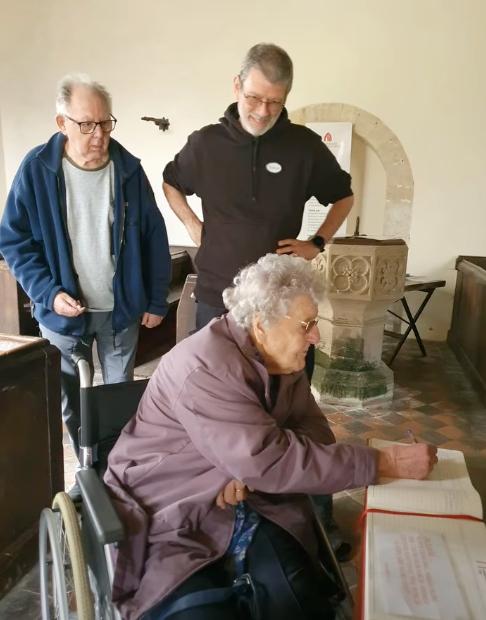 older lady writing in a book while other people watch
