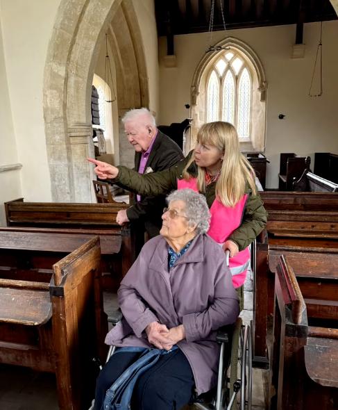 older lady being pushed in a wheelchair with another older man looking around a church